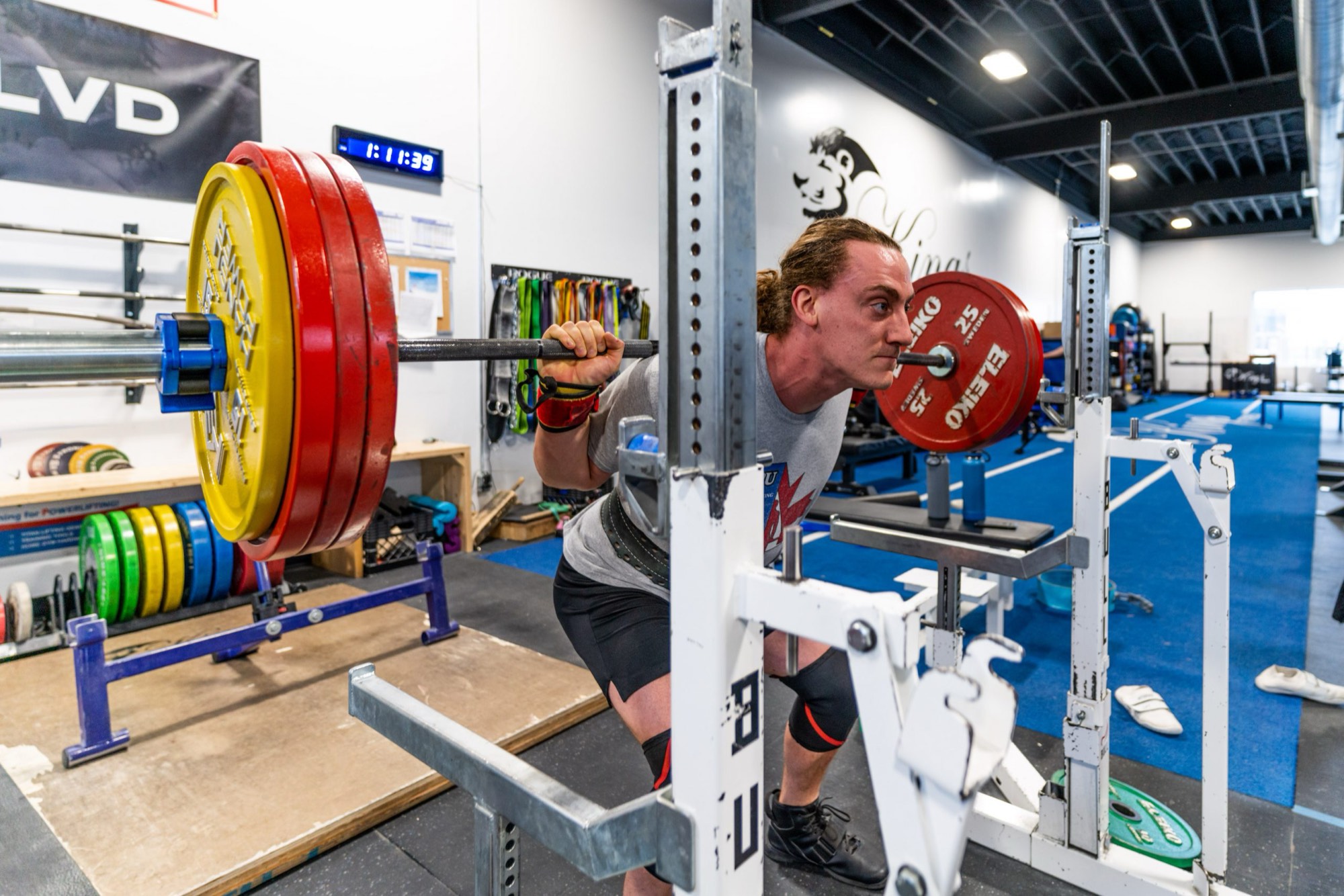 A lifter walks out a loaded squat bar under the Kings Fitness lion mural